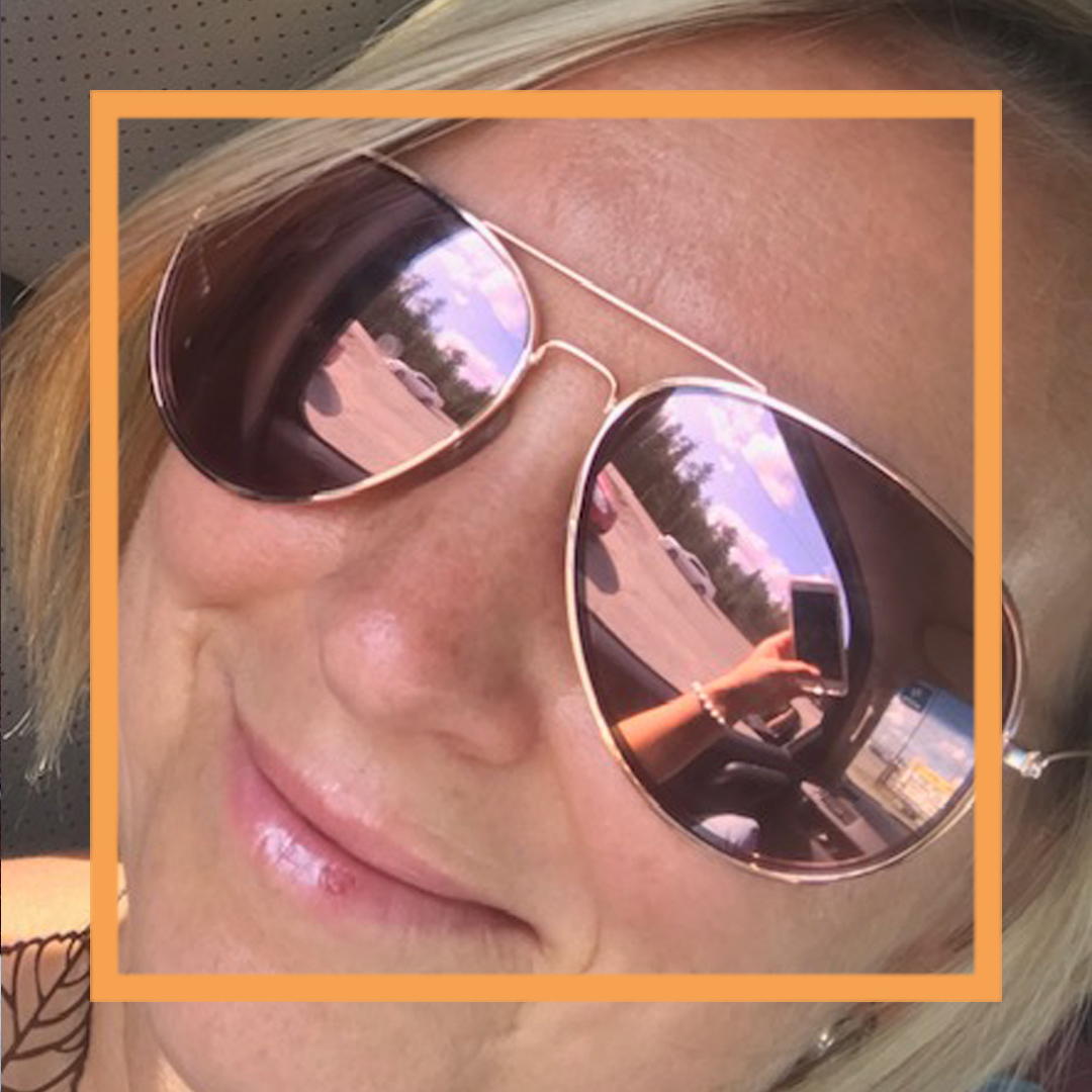 A closeup up of Chrystal smiling at the camera and wearing aviator sunglasses. There is a thin orange box framing the photo.