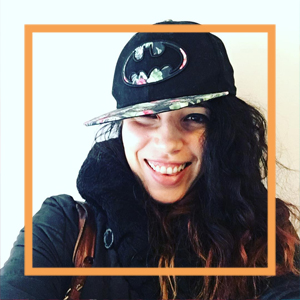 Nicole wears a flatbrimmed black cap with the batman logo and smiles at the camera