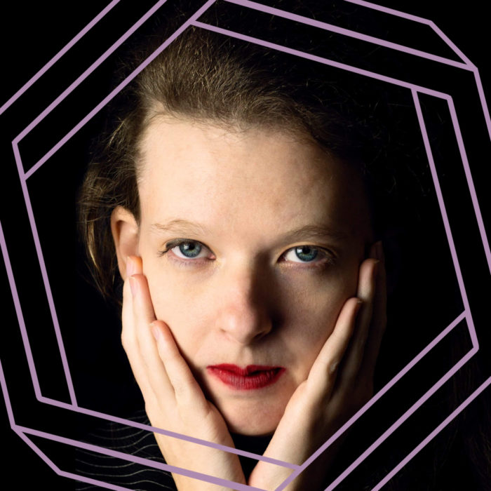 Belle is wearing bright red lipstick and looking at the camera while she rests her chin on her hands. There is a stylized purple hexagon superimposed around her face.
