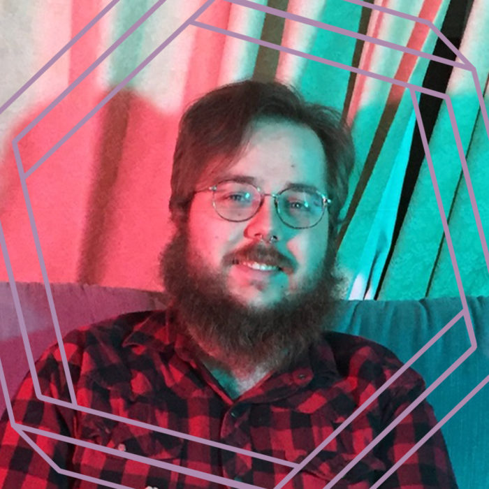 David, a white man with glasses and a beard, smiles at the camera. There is a stylized purple hexagon framing the photo.