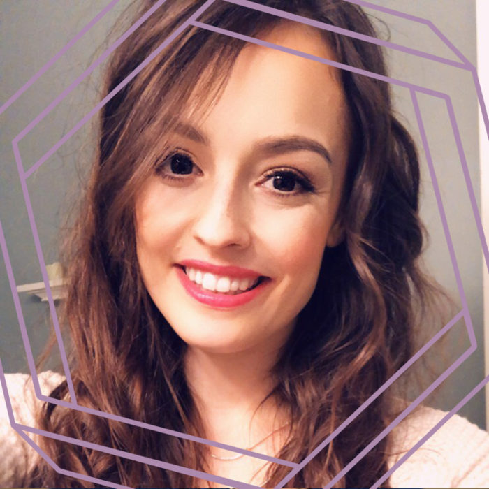 Emily, a white woman with long wavy brown hair, smiles at the camera. There is a stylized purple octagon superimposed around her face.