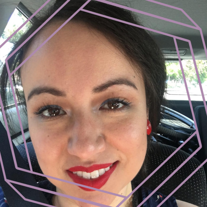 Felisha, wearing red lipstick with her hair tied back in a ponytail, is smiling at the camera. There is a stylized purple hexagon superimposed over the photo.