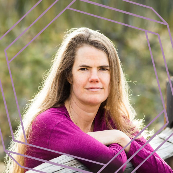 Julie is wearing a magenta sweater and leaning on a split rail fence. She is standing in the sun and looking straight at the camera. There is a stylized purple octagon superimposed over the photo.
