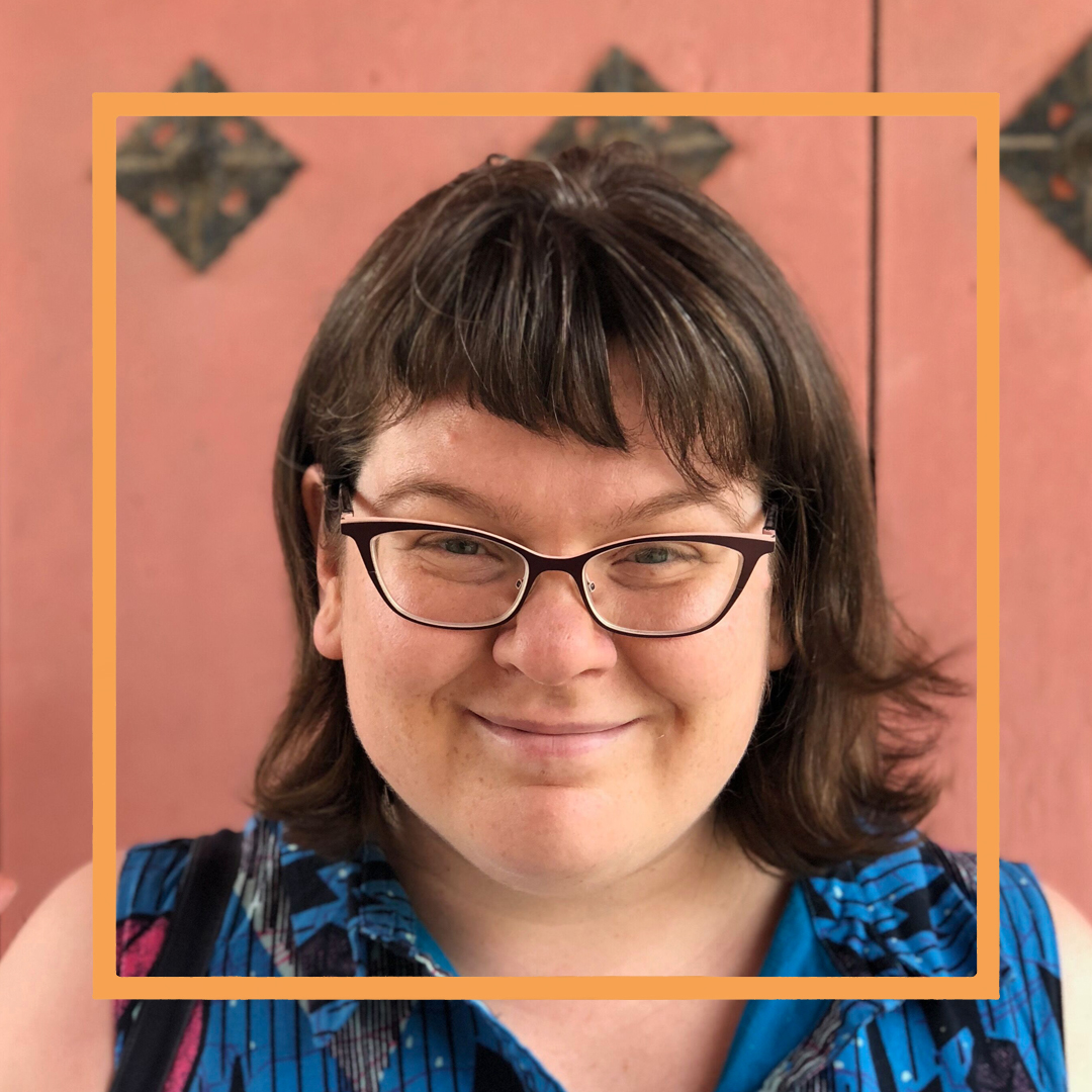 Meredith, a white woman with shoulder-length brown hair and black framed glasses, smiles at the camera. There is an orange square superimposed over her face.