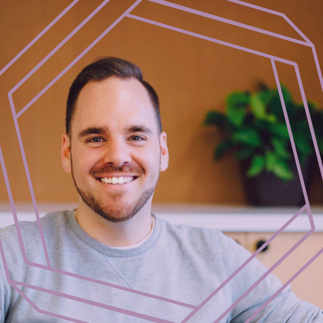 Stuart, a white man with short brown hair and close-cut facial hair, smiles at the camera. There is a stylized purple hexagon framing the photo.