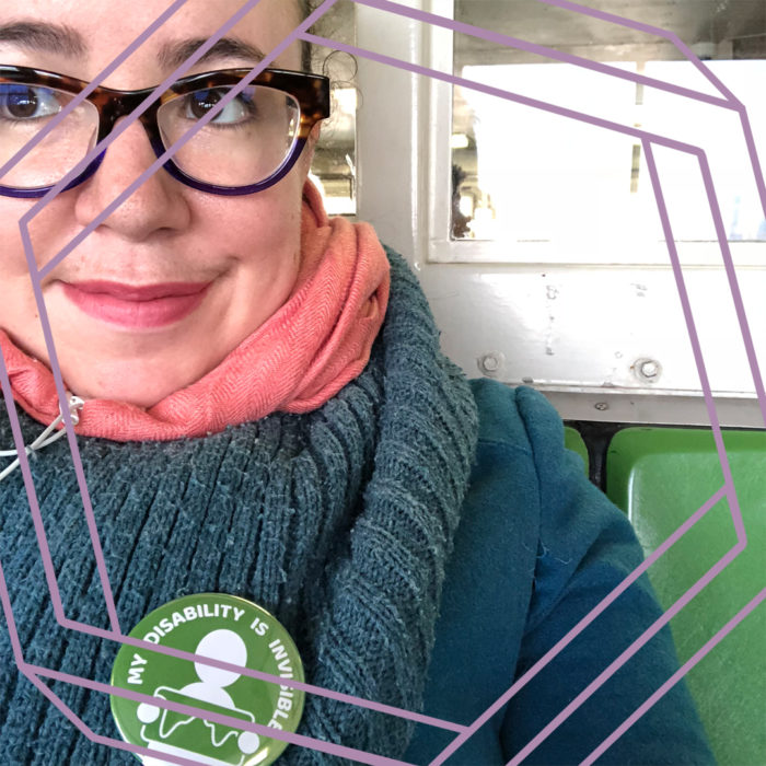 A close-cropped photo of Tema's face and shoulders. She is wearing tortoise shell glasses and looking off camera, and wearing a thick wool scarf with a green button that reads "My disability is invisible." There is a stylized purple hexagon superimposed over the photo.