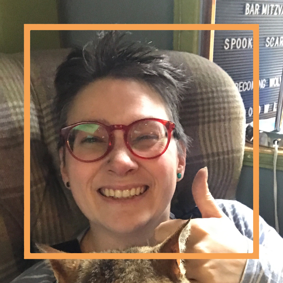 Marie, a whit woman with short dark hair and red framed glasses is smiling at the camera and giving a thumbs up. There is an orange box superimposed over the photo.