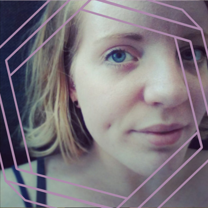 Annie, a white woman with blonde or auburn shoulder-length hair, looks at the camera. The photo is cropped close around her face and framed by a purple hexagon.