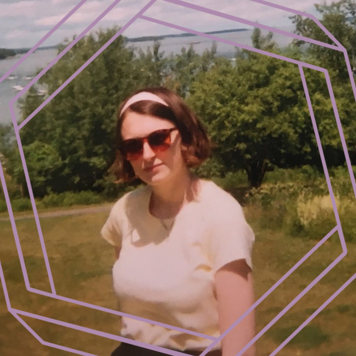 Olivia, a white woman wearing sunglasses, a light headband, and a yellow tshirt, looks at the camera. There is greenery and open water in the background. There is a purple hexagon superimposed over the photo.