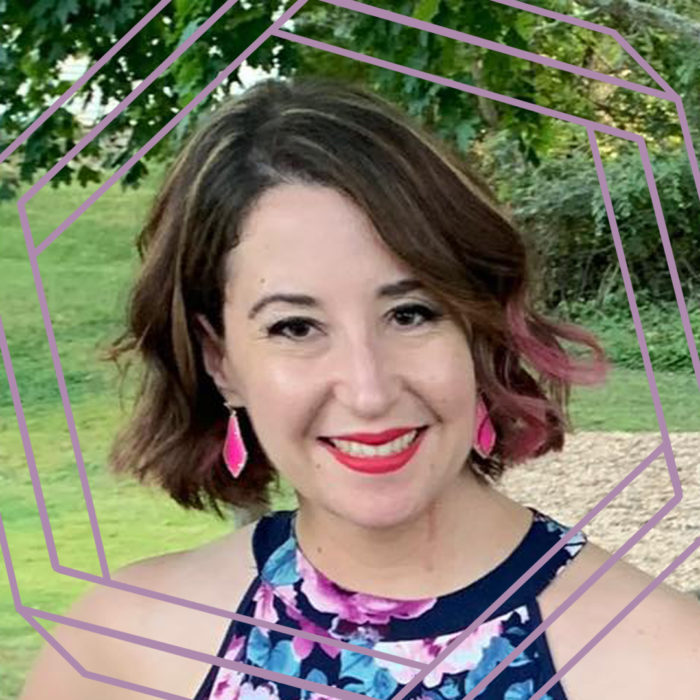 Jenna, a white woman with a wavy brown bob that has pink and blond streaks, smiles at the camera. Jenna is wearing pink earrings, red lipstick, and a sleeveless floral top. There is grass and trees in the background and there is a stylized purple hexagon framing the photo.