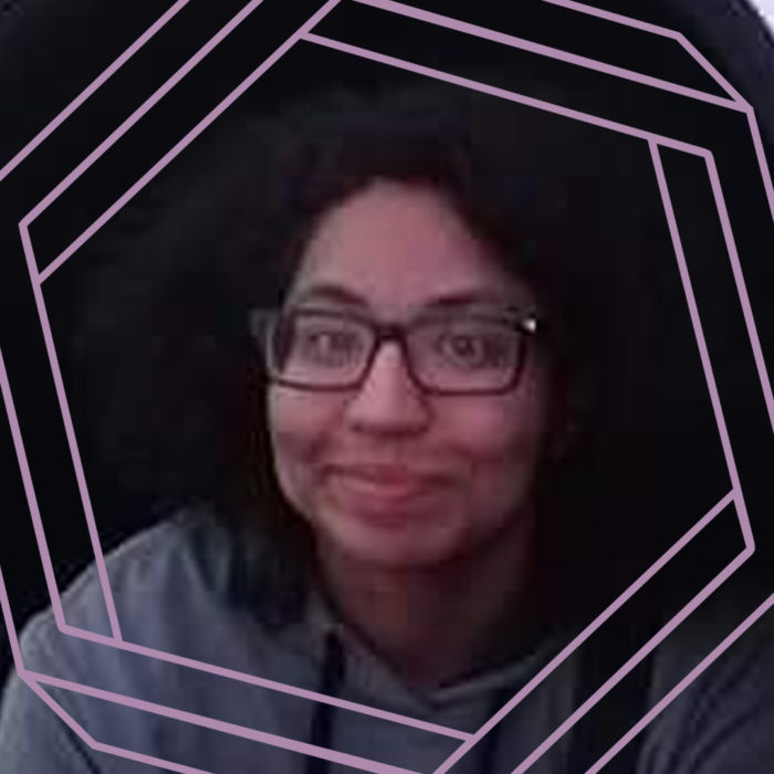 Valerie, a woman with curly black hair and glasses smiles at the camera. There is a stylized purple hexagon framing the photo.
