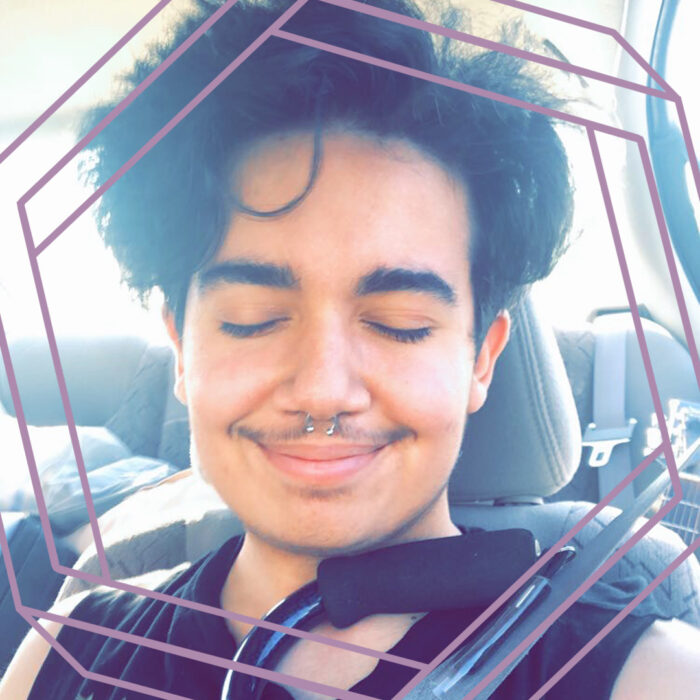 Drew is a latinx person with light brown skin and short black hair. His septum is pierced with a silver hoop. In this photo he is sitting in the front seat of a car, smiling with his eyes closed. He is wearing a black tank top and proudly holding up a cane. There is a stylized purple hexagon framing the photo.